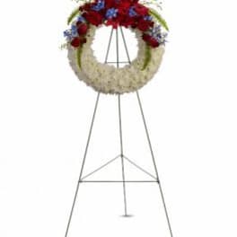 Standing funeral wreath with red, white, and blue flowers on an easel