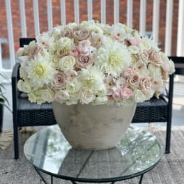 Large pastel floral arrangement in a stone vase on a glass table