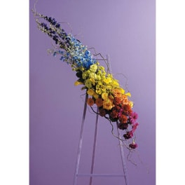 Rainbow floral arrangement on a clear stand against a lavender background