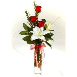 Red roses and a white lily in a clear vase with a red ribbon