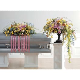 Two pastel floral sprays on a casket, one with pink ribbons.