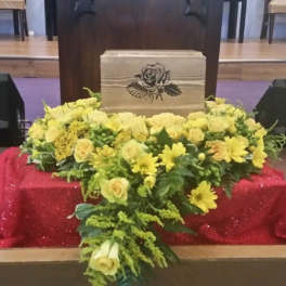 Yellow floral arrangement around a wooden urn with a rose emblem
