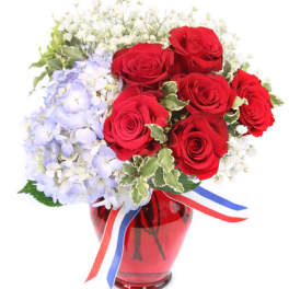 Red roses and pale blue hydrangeas in a red vase with ribbon