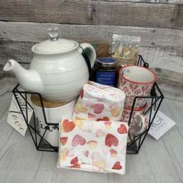 Gift basket with a teapot, mug, honey, and heart-patterned towels