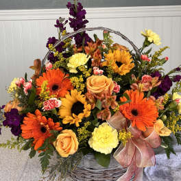 Basket arrangement of orange and yellow flowers with purple accents and a ribbon