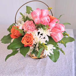 Basket arrangement of orange and white flowers with pink ribbon bows