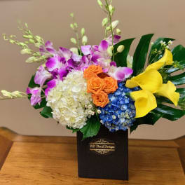 Colorful floral arrangement in a black box with orchids, hydrangeas, roses, and calla lilies