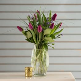 Pink tulips in a clear glass vase with a small gold candle holder