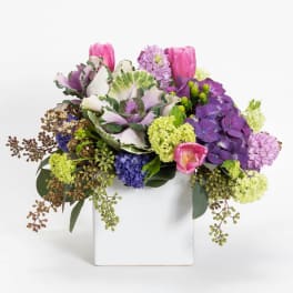 Colorful bouquet in a white square vase with pink, purple, and green blooms