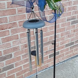 Wind chime with blue ribbon and greenery on a metal stand