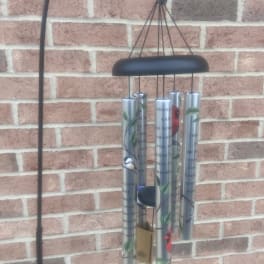 Black metal wind chime with silver tubes hanging against a brick wall