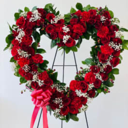 Heart-shaped red rose wreath on a stand with a pink ribbon bow