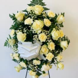 White floral funeral wreath on a stand with a ribbon bow