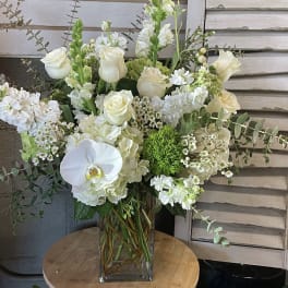 White floral arrangement in a clear glass vase with roses and orchids