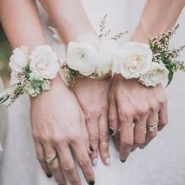 Hands wearing white floral wrist corsages with small white blooms