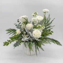 White roses and ranunculus in a white vase with mixed greenery
