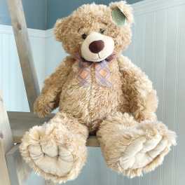 Large plush teddy bear with a plaid bow sitting on a wooden ladder