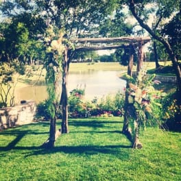 Floral-decorated wooden arch on a grassy lawn by the water
