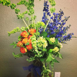 Tall bouquet of orange roses and blue delphinium in a glass vase