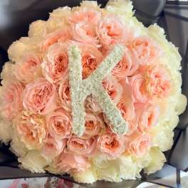 Round bouquet of peach and cream roses with a white letter K