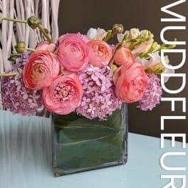 Pink ranunculus and lilac hydrangeas in a square glass vase
