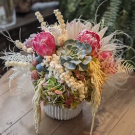 Pink protea and succulents arranged in a white vase
