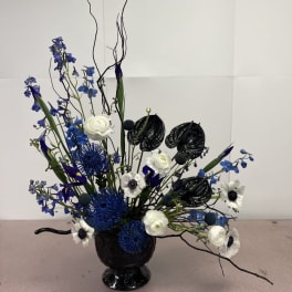Blue and white floral arrangement in a black vase with tall curly branches