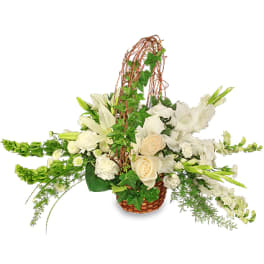White lilies, roses, and other blooms in a long wicker basket with an arching twig handle.