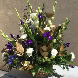 Tall floral arrangement with white and purple blooms in a wicker basket