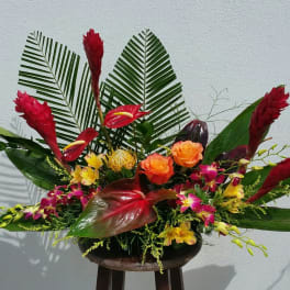 Tropical flower arrangement with red and orange blooms in a low container