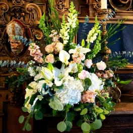 Large white floral arrangement with lilies, calla lilies, and pastel blooms