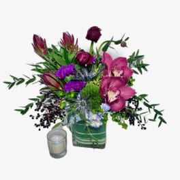 Purple floral arrangement in a square glass vase with a small candle