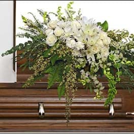 White floral casket spray with cascading greenery on a wooden casket