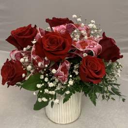Red roses arranged in a striped white vase with pink ribbon and baby's breath