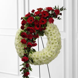 Standing white wreath with cascading red roses, gerbera daisies, and carnations on a metal easel