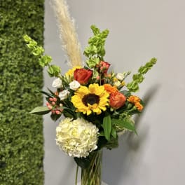 Mixed bouquet in a clear glass vase with sunflowers, roses, hydrangea, and orange blooms