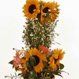 Tall arrangement of yellow sunflowers with pink accents in a container against a light background