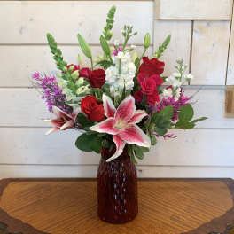 Red roses and pink lilies arranged in a dark glass vase