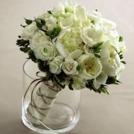 Round white rose bridal bouquet resting in a clear glass cylinder vase