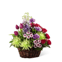 Basket arrangement with red roses, purple tulips, lavender carnations, and green spider mums.