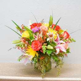 Mixed bouquet of roses, lilies, and yellow blooms in a glass vase