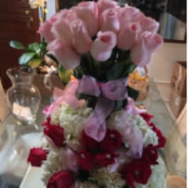 Tall arrangement of pink roses above a dome of white blooms with red roses and pink ribbon
