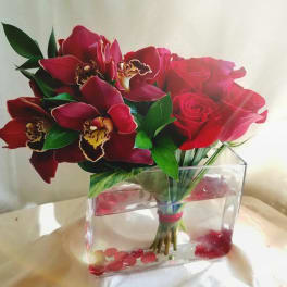 Red roses and orchids arranged in a clear rectangular vase