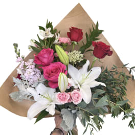 Bouquet of red and pink roses with white lilies and greenery in brown paper