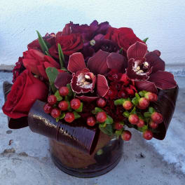 Red and burgundy floral arrangement in a dark glass vase