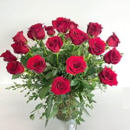 Bouquet of red roses in a clear glass vase with a small candle nearby