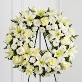 White floral wreath with lilies and roses on a black stand