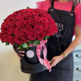 Large red rose arrangement in a black hatbox with a pink ribbon