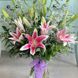 Pink stargazer lilies in a glass vase with a purple ribbon