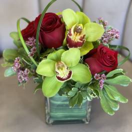 Red roses and green orchids arranged in a square glass vase